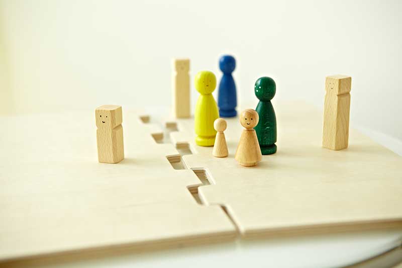 Symbolisches Gruppenbild mit Holzfiguren – Darstellung von Distanz und Beziehung in der Kinder- und Jugendpsychiatrie. Über uns, Praxis Schneider und Team, Kinder- und Jugendpsychiatrie Köln.